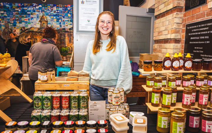 A women stands at a farmer's market booth selling honey 